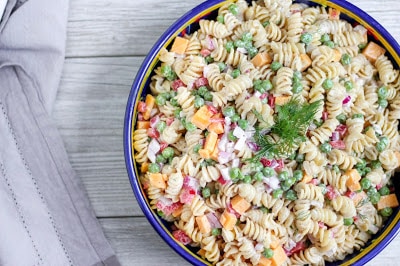 overhead shot of the pasta salad in a blue rimmed bowl on a pale grey wood surface and a grey linen.