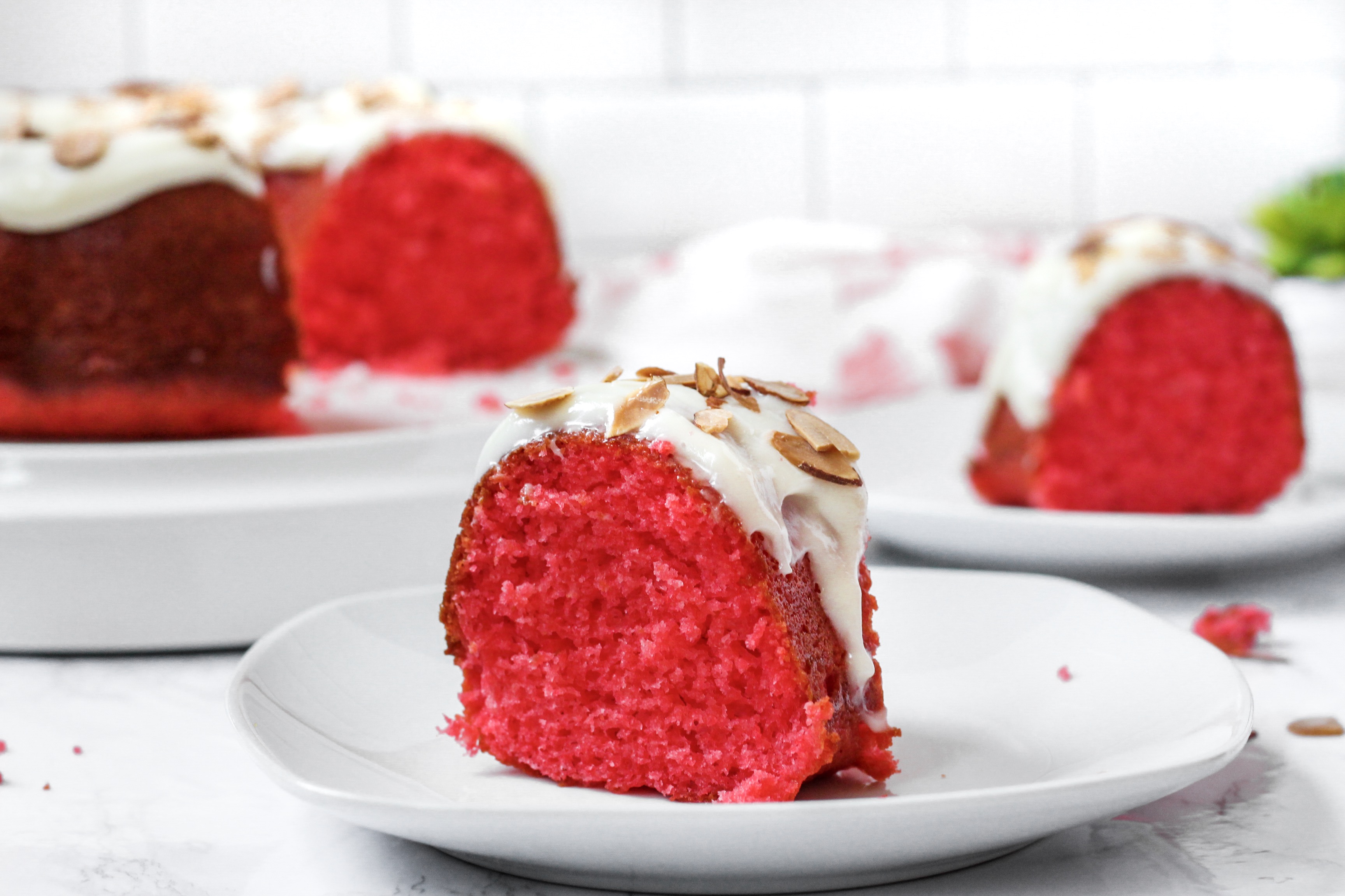 A slice of the raspberry cake, a slice in the background along with the whole cake.