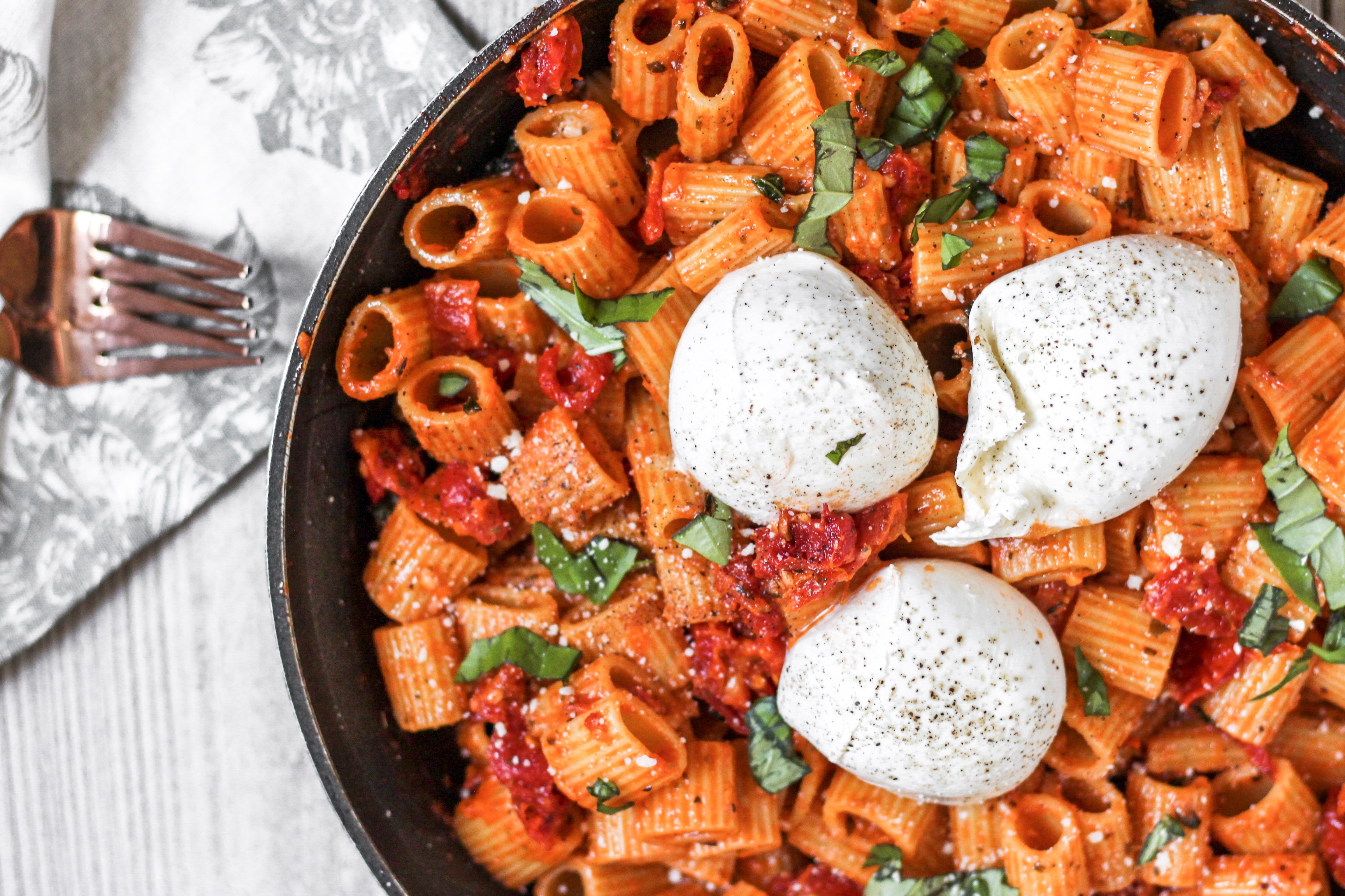 overhead shot of the pasta in a pan with 3 balls of Burrata, a floral linen napkin and 2 forks.