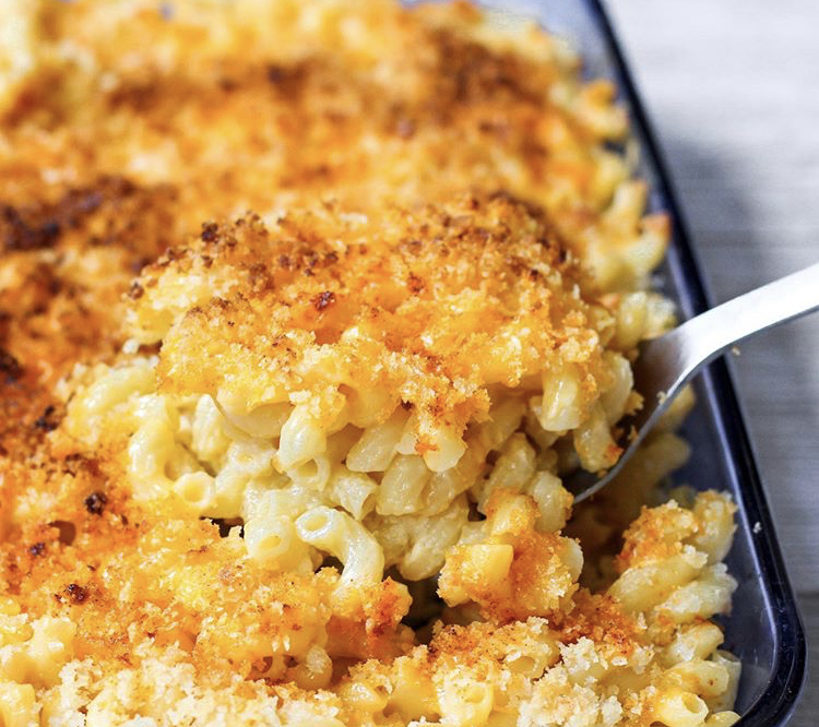 a spoon scooping the mac and cheese from a blue casserole dish.