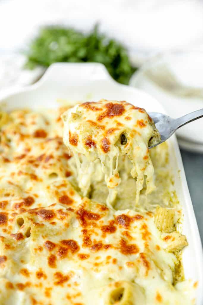 scooping the chicken pesto pasta bake from the white casserole dish