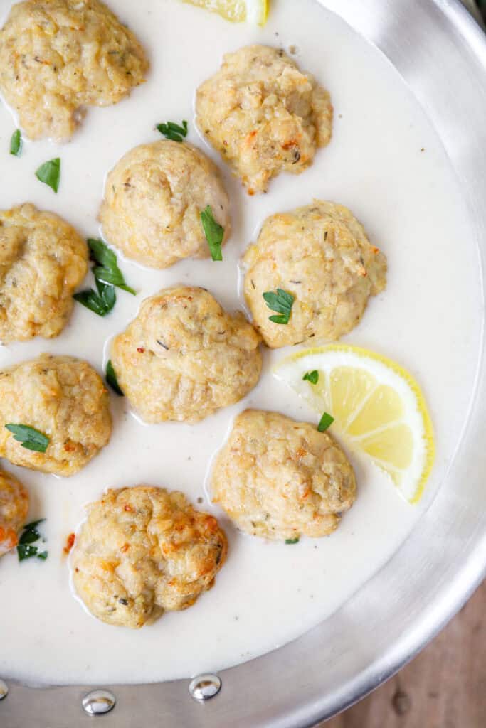 overhead photo of the chicken piccata meatballs with lemon wedges in a stainless steel pan.