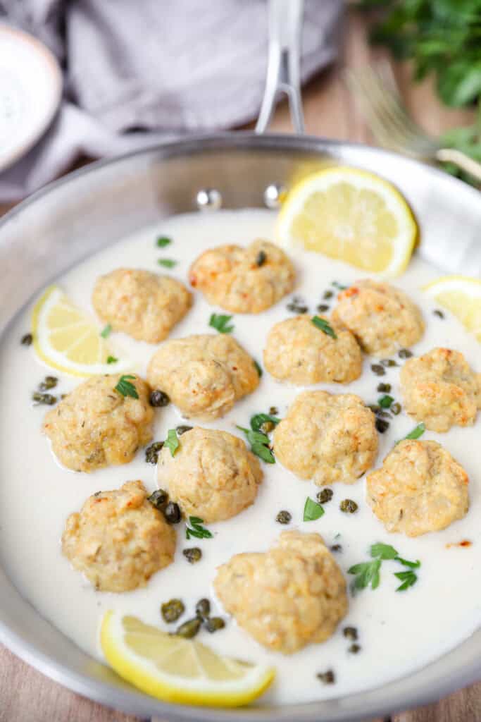 chicken meatballs in the lemon piccata sauce with fried capers and parsley in a stainless steel pan.