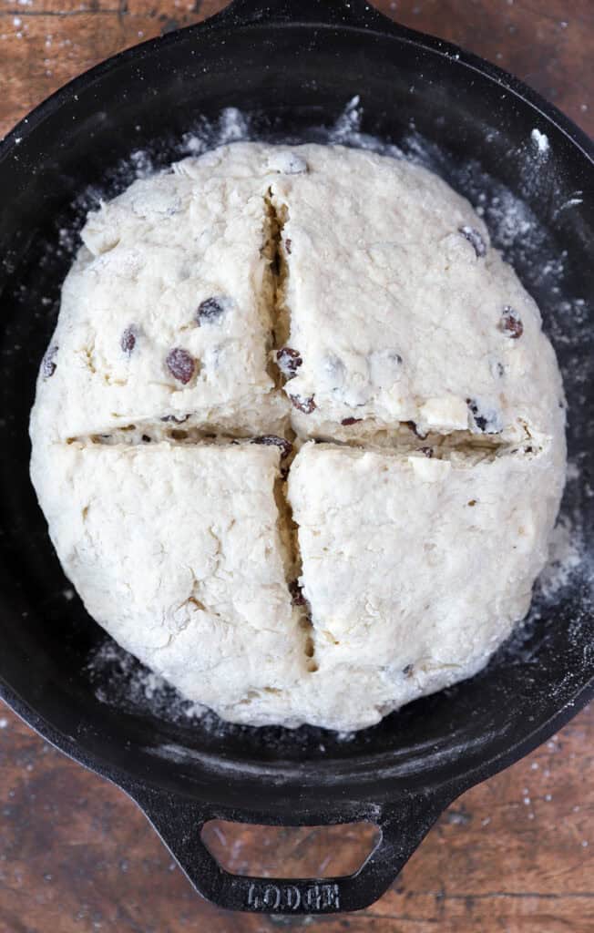 overhead photo of the bread dough with an X cut into the top in a cast iron skillet.