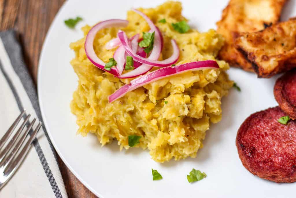 Close shot of mangu with pickled red onions and fried cheese and fried salami.