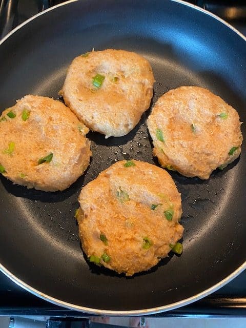 4 of the chicken burger patties in the frying pan cooking. 