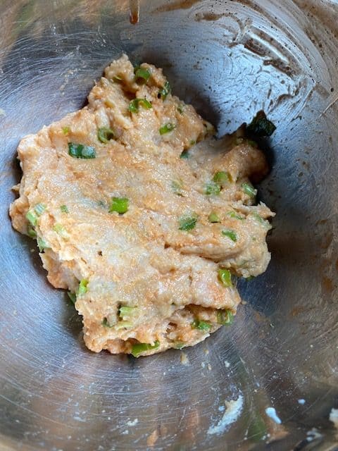 A silver mixing bowl with the raw ground chicken mixture.