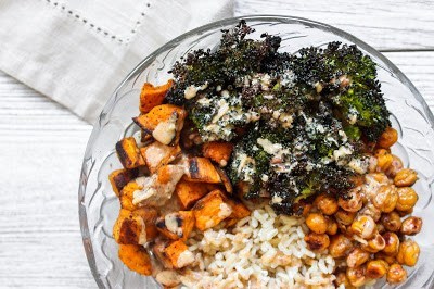 Overhead shot of a glass bowl with roasted sweet potatoes, roasted broccoli, crispy chickpeas, and rice covered in a tahini dressing.