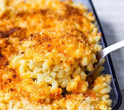 A large spoon scooping the macaroni and cheese from a blue casserole dish.