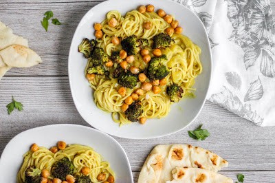 Overhead shot of two bowls of a creamy curry pasta with crispy chickpeas, broccoli and naas. A grey floral napkin on the side