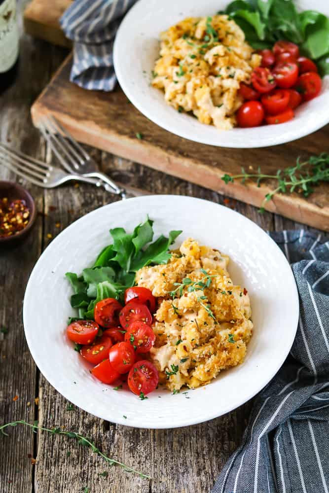 vegan mac and cheese with tomatoes in a white bowl on a wood board.