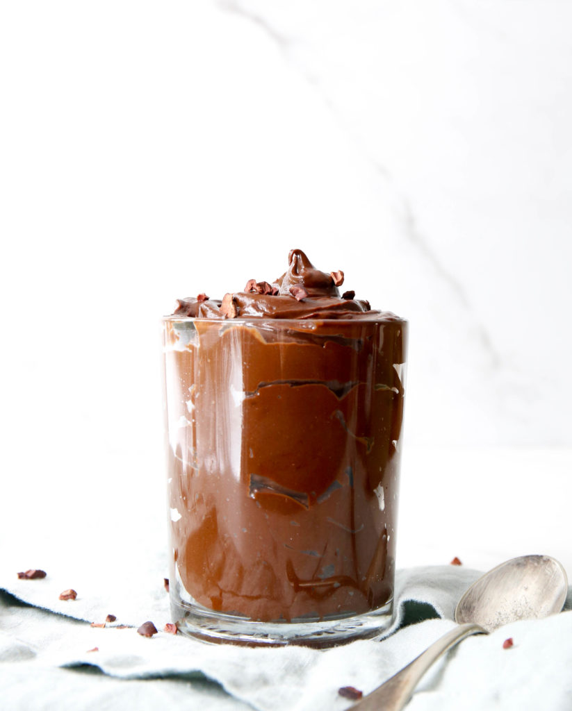 a clear glass filled with the chocolate avocado mousse with a spoon.