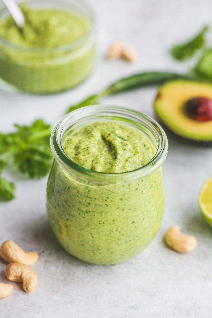 a jar of the avocado cilantro dressing with cashews scattered about, parsley, on a grey concrete surface.