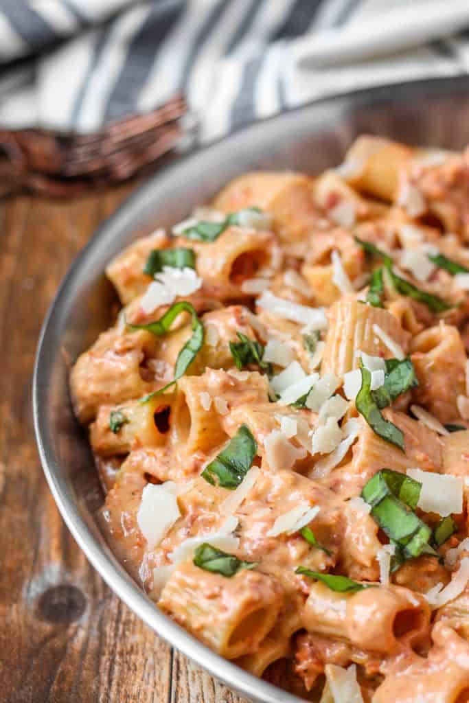 creamy sun dried tomato pasta in a silver pan on a wood pattern surface.