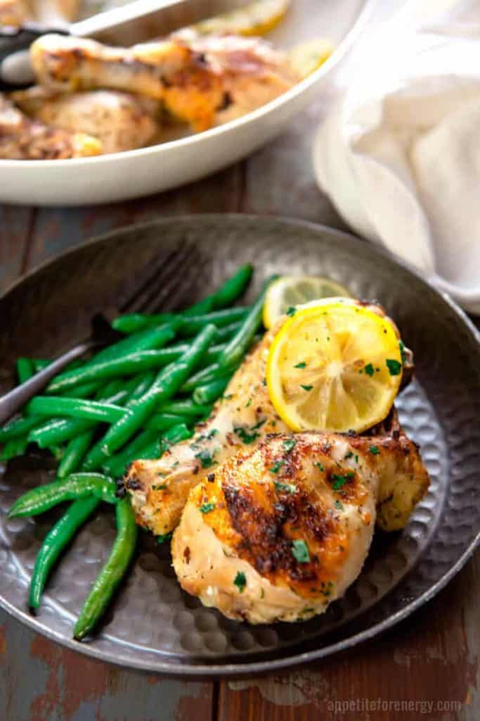 herb roasted drumsticks on a plate with green beans and lemons.