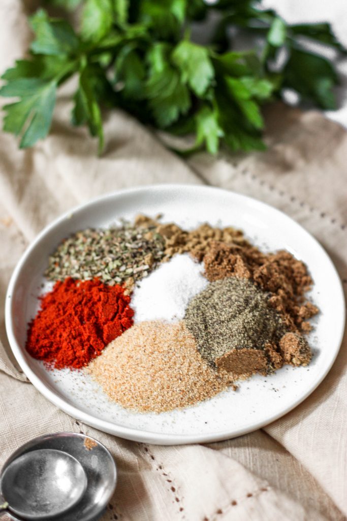 a white plate with the sazon spices unmixed. Measuring spoons in the front and parsley in the back.