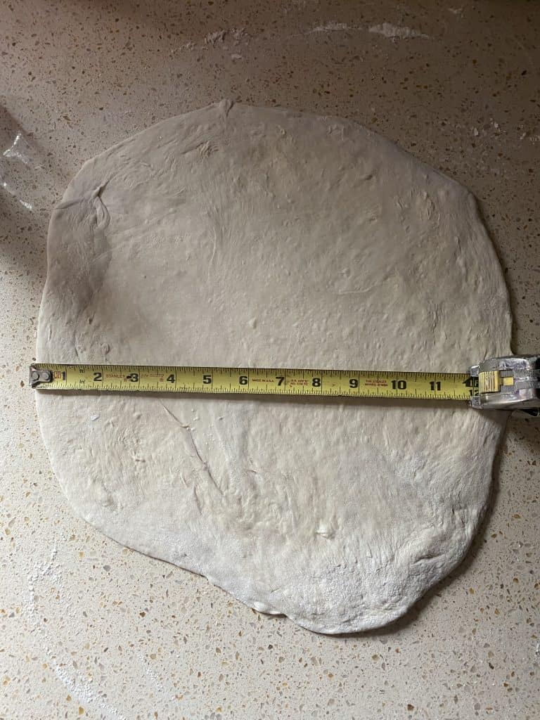 raw dough on a countertop rolled into a 12" circle with a tape measure showing it's 12" wide.