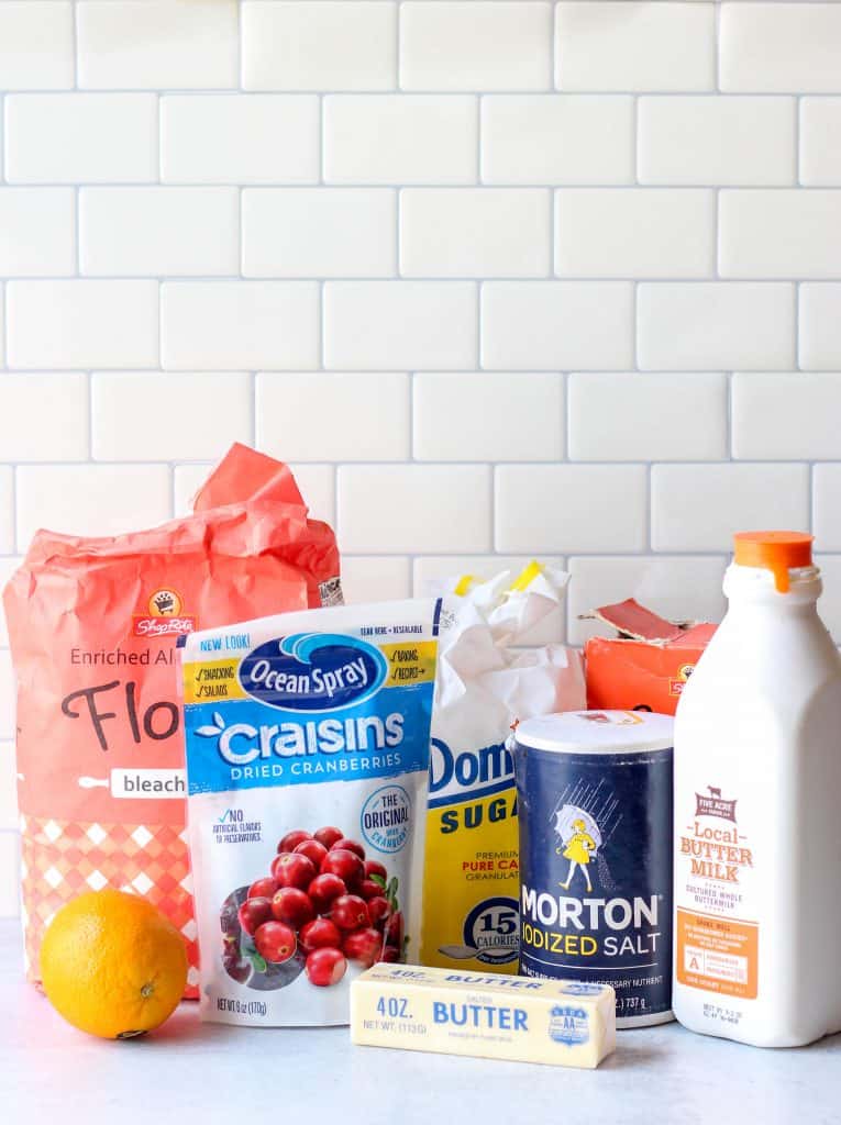 ingredients, a bag of flour, a bag of dried cranberries, a bag of sugar, a stick of butter, an orange, a box of baking soda, salt, and buttermilk.