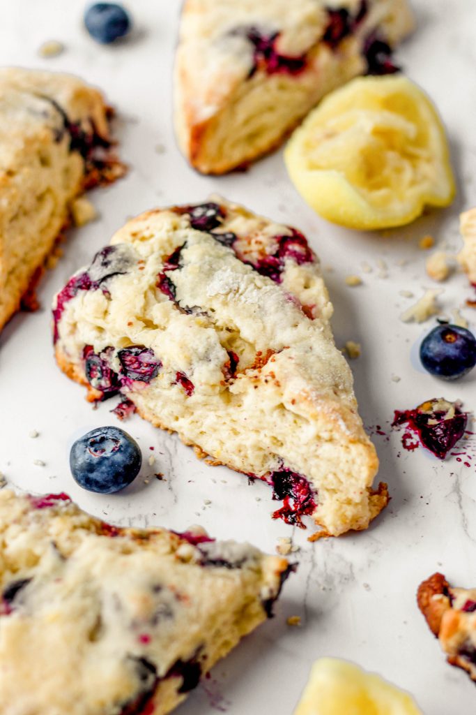 lemon blueberry scones on a white marble surface with blueberries and lemons.