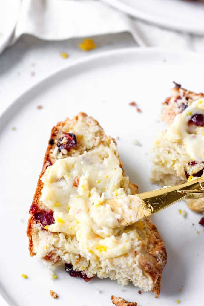 a slice of the bread with a gold spreading knife spreading the orange butter.