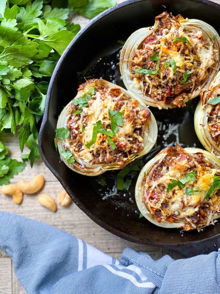 overhead shot of sausage stuffed onions in a cast iron skillet with parsley and garlic cloves behind the skillet.