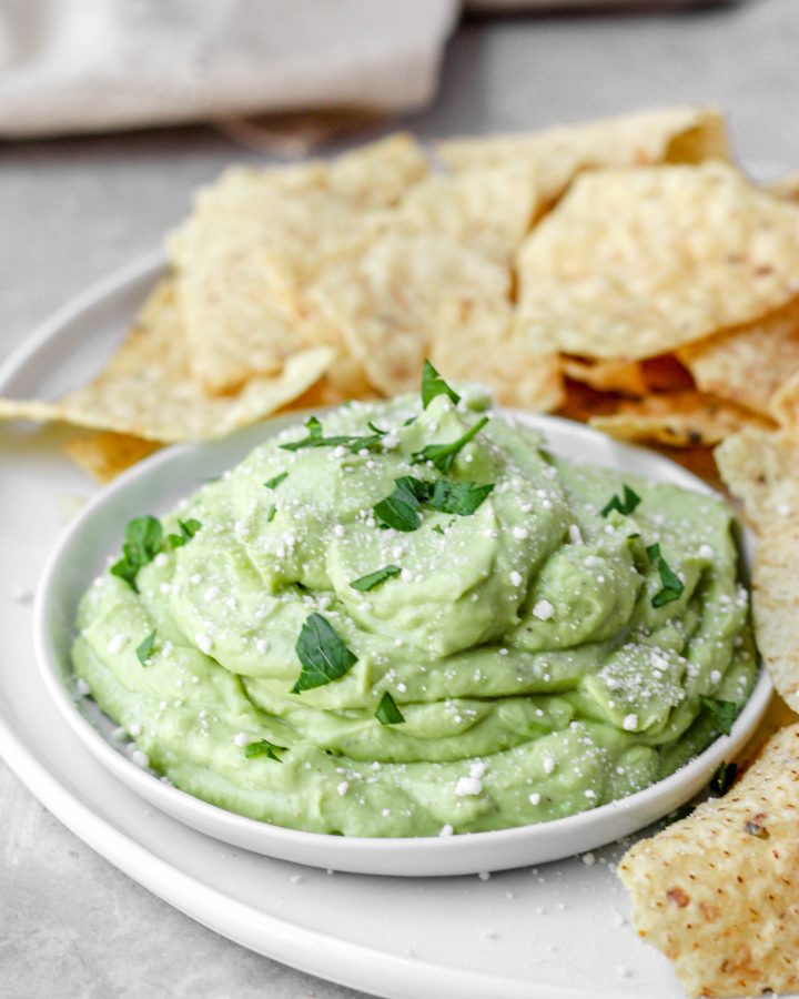 A small round plate with the whipped avocado dip on a plate of chips.