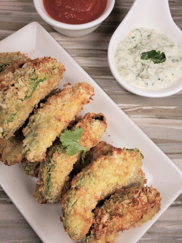 overhead sot of avocado fries on a rectangle plate, a dipped sauce in the back.