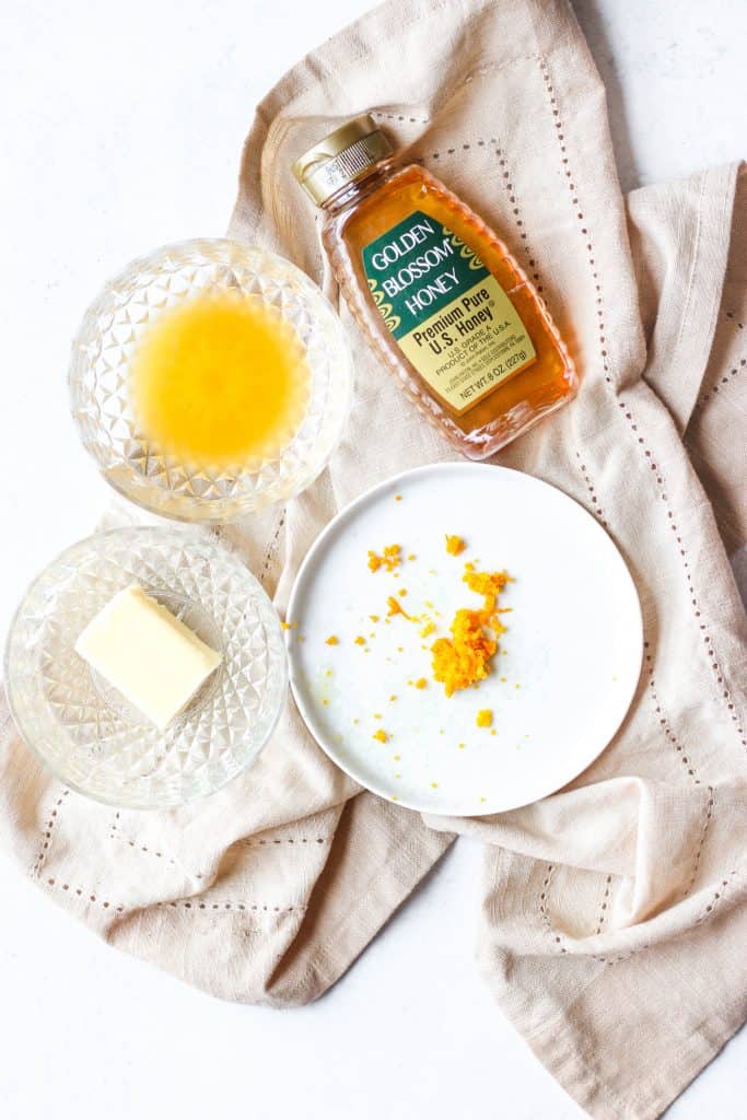 overhead shot of the ingredients a bowl of OJ, a plate of orange zest, butter, and honey.