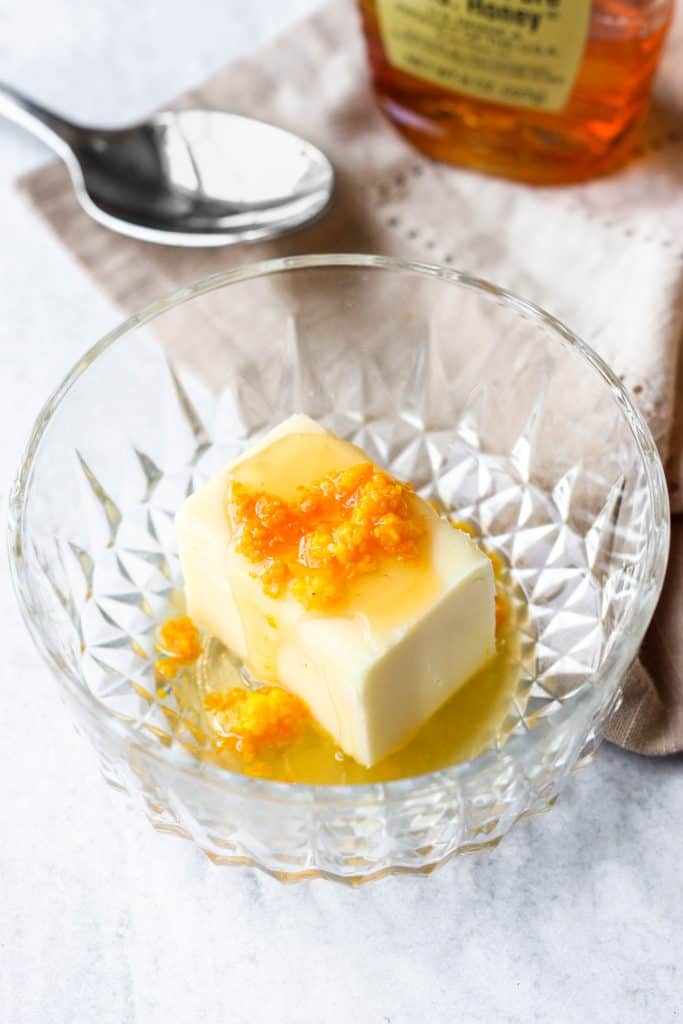 the ingredients in a bowl before mixing, the stick of butter with the zest, honey, and juice on top.