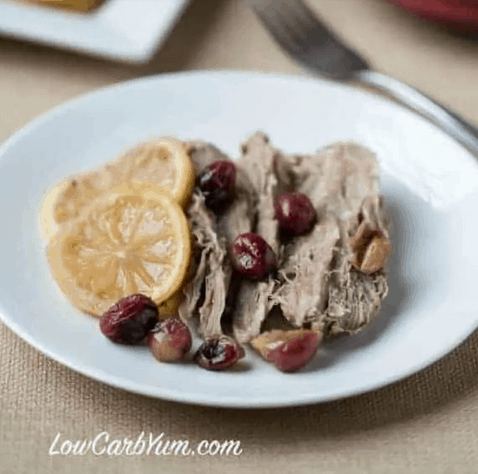 pork roast with whole cranberries and lemon wedges on a white plate.