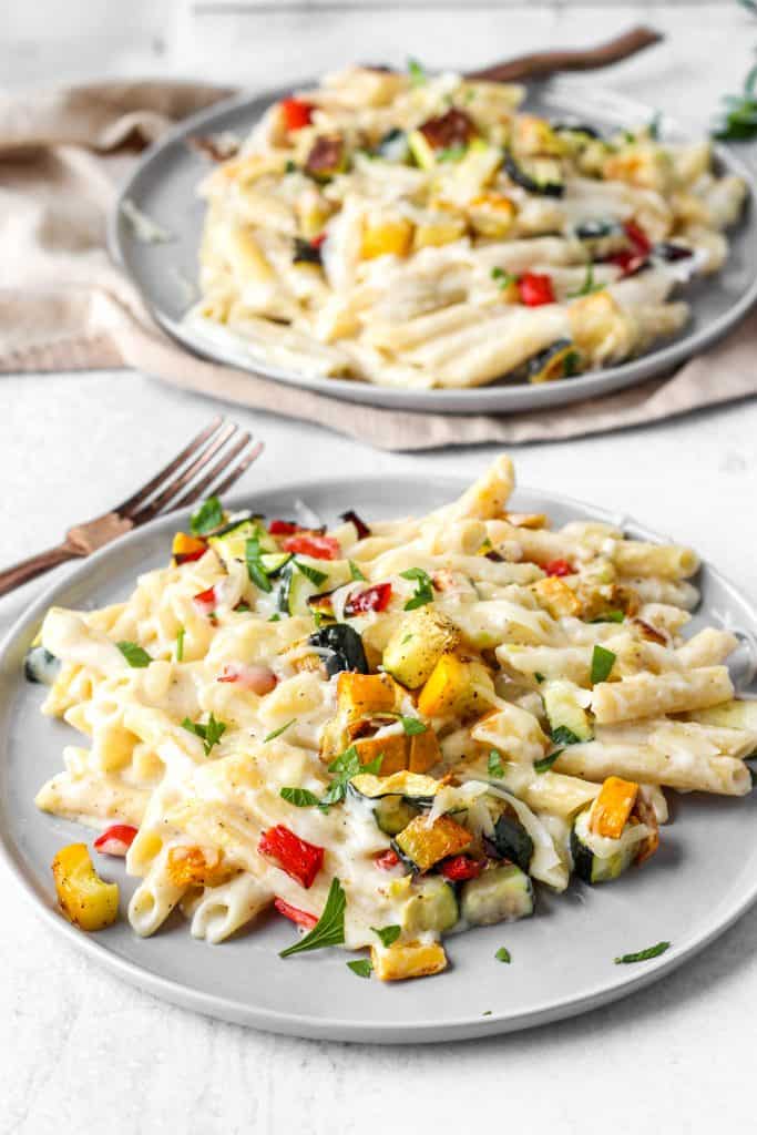 two grey plates with the creamy vegetable pasta with a fork