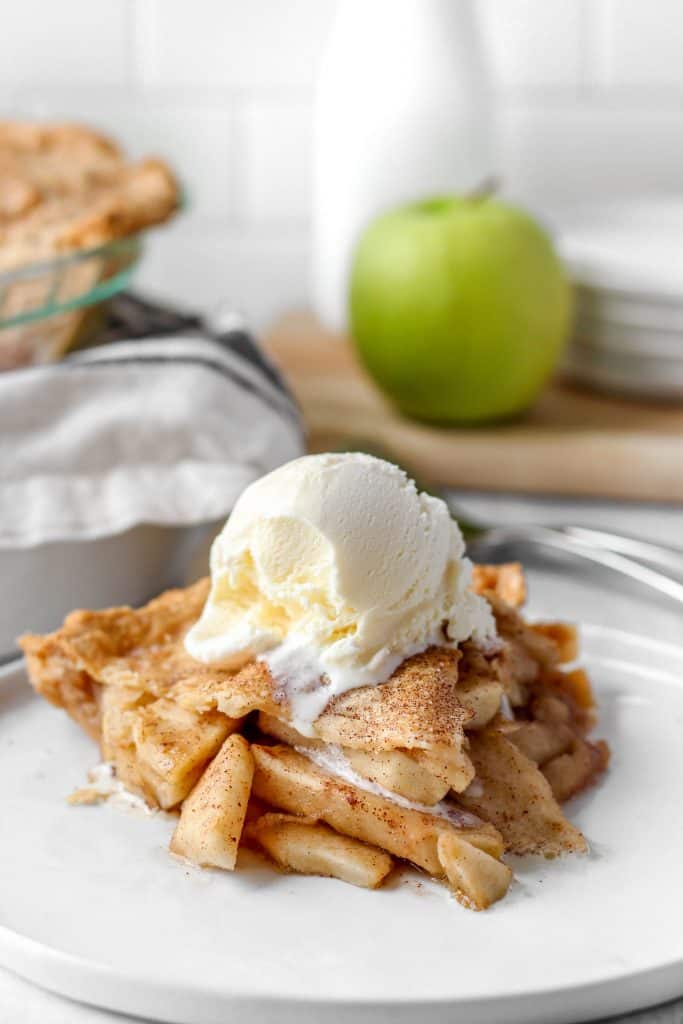 apple pie with a scoop of vanilla ice cream, the whole pie in the background.