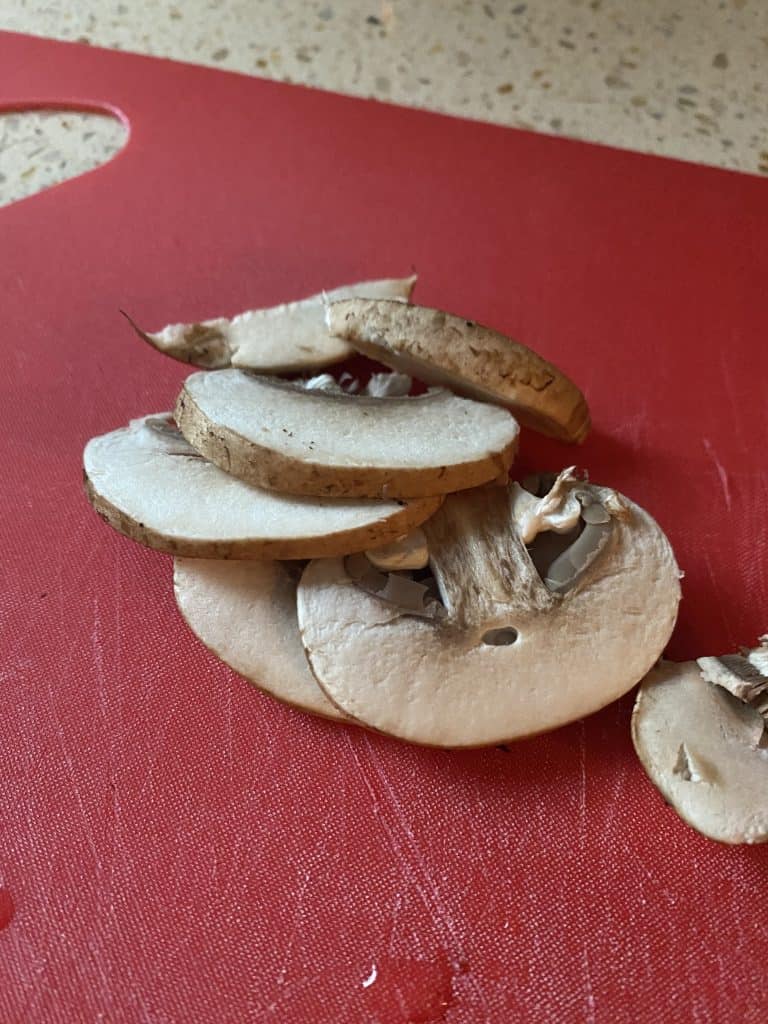 close shot of sliced uncooked mushrooms on a red cutting board.