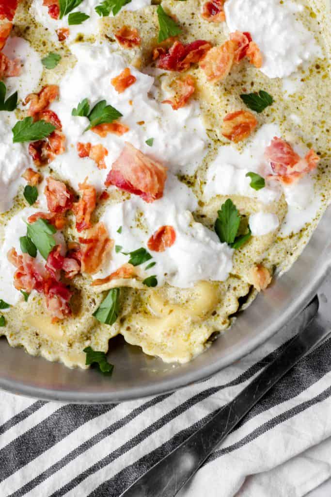 creamy pesto sauce ravioli with pancetta and burrata in a pan with parsley.