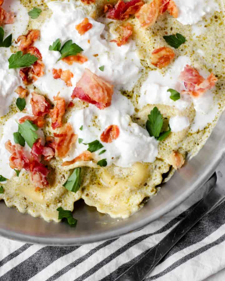 creamy pesto sauce ravioli with pancetta and burrata in a pan with parsley.