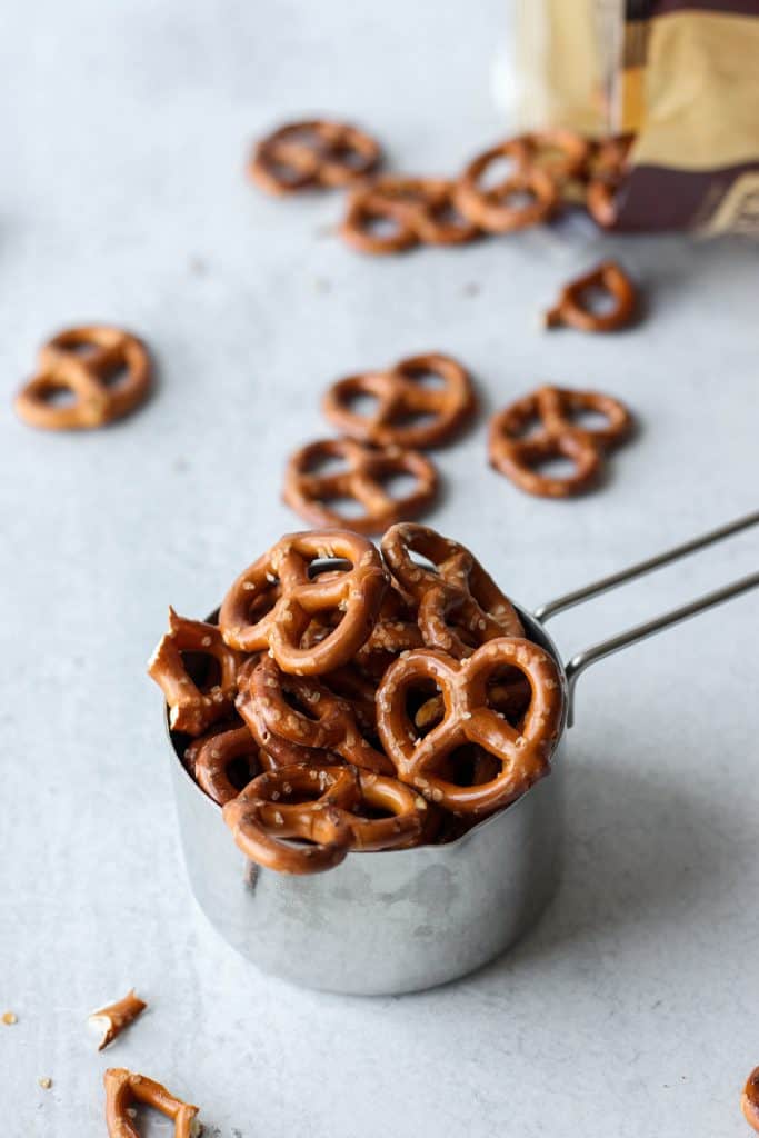 mini pretzels in a silver measuring cup on a cement pattern board.