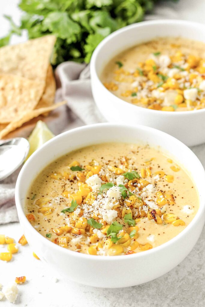 two bowls of creamy Mexican corn chowder with chips and parsley in the back.