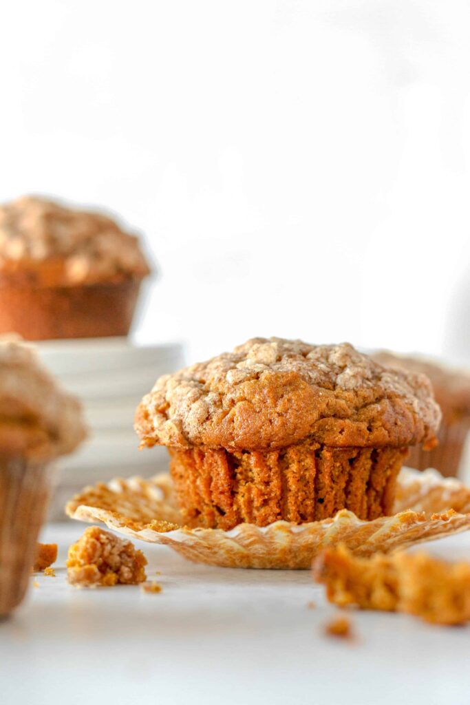 a pumpkin muffin with the wrapper unwrapped...a few stacked plates in the background with a muffin on top.