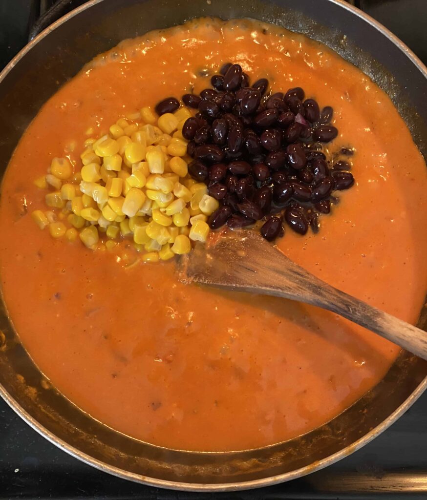 overhead shot of the pan with the creamy pasta sauce with the corn and beans being mixed in. 
