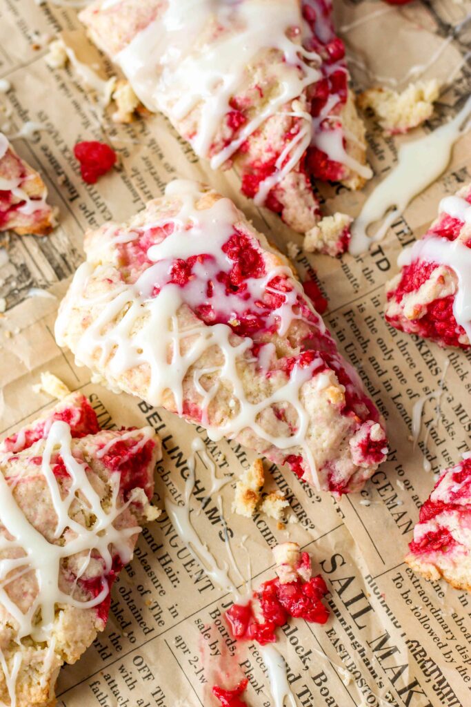 overhead shot of the raspberry scones with white chocolate drizzle on beige newsprint food paper.