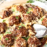 the french onion meatballs in a glass circular baking dish with a silver spoon scooping.