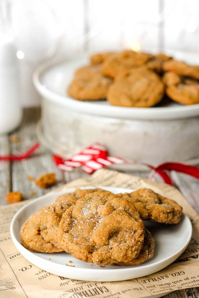 a plate of molasses cookies with red wrapping ribbon in the background with a plate of more cookies.