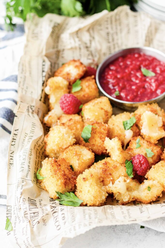 side view of the platter of cheese bites. blurred parsley and the sauce in the background. 