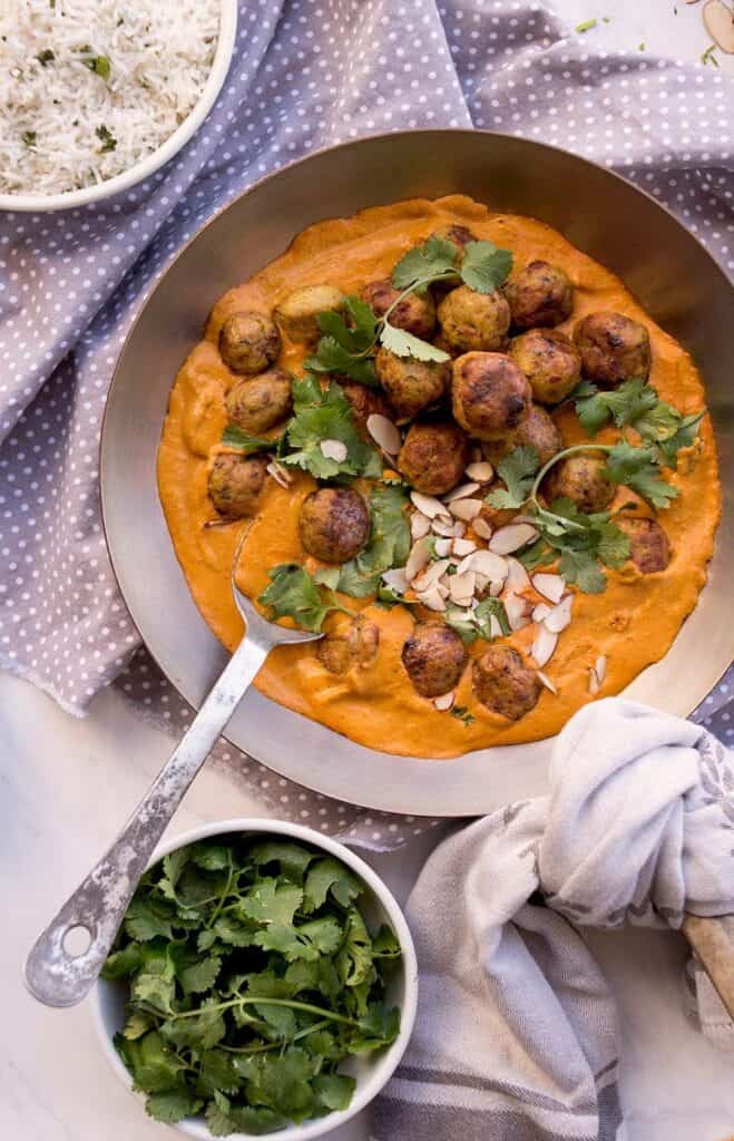 butter chicken meatballs in a bowl with a large spoon and a grey and white polka dot napkin.