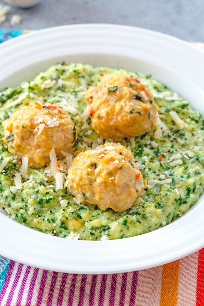 three chicken meatballs on kale polenta in a white bowl.