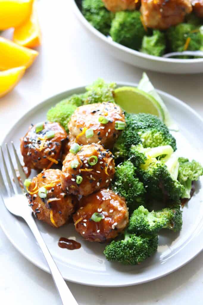 orange chicken meatballs with a fork, broccoli and lime wedge.