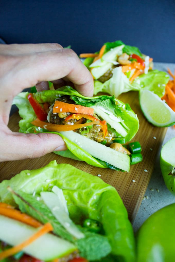 chicken meatballs in a lettuce wrap on a wood cutting board with a hand grabbing the lettuce wrap.