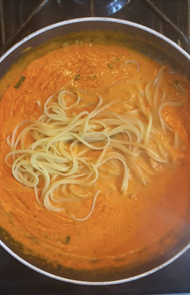 overhead photo of the pan with the completed creamy roasted red pepper sauce with the linguini pasta being add in.