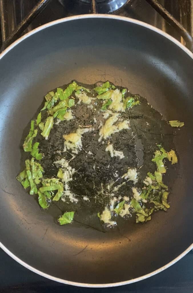 overhead photo of a pan with oil, grated garlic, and chopped basil.