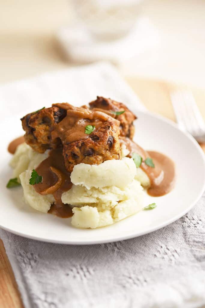 chicken marsala meatballs on mashed potatoes on a white plate.
